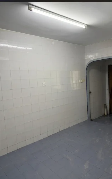 Room features: white tiled walls, blue tiled flooring, fluorescent ceiling light, arched doorway, empty space.